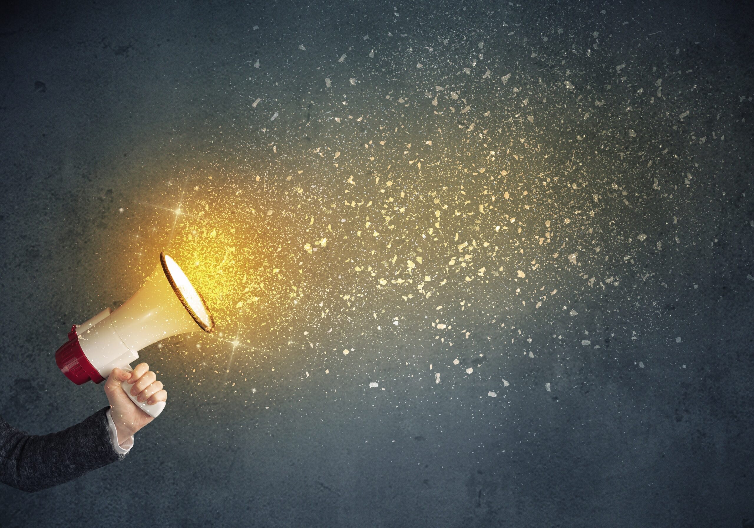 Hand holding megaphone with sparkles coming out of the speaker