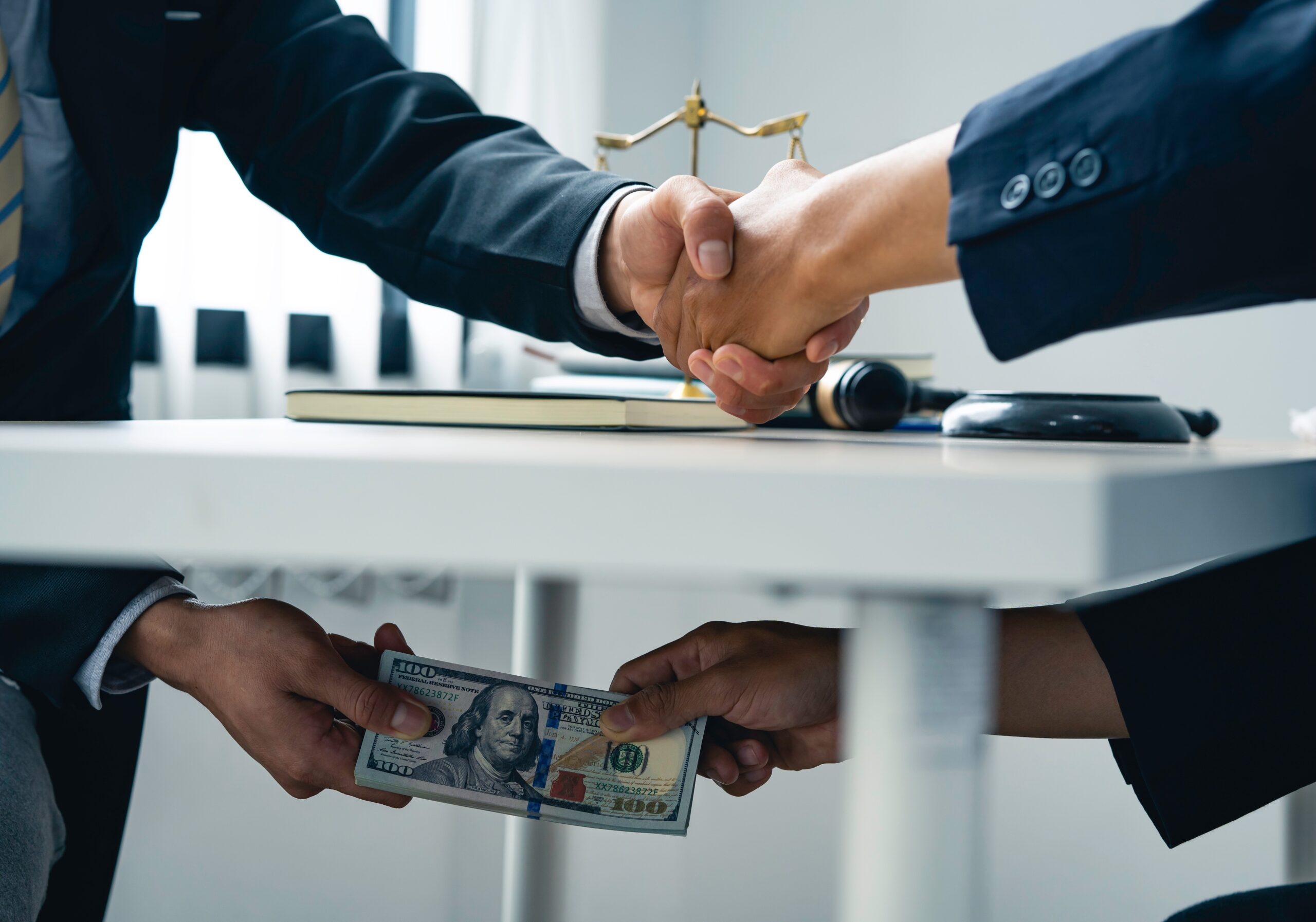 amrs of business people shaking hands above the talbe and transferring cash under-the-table bribe to