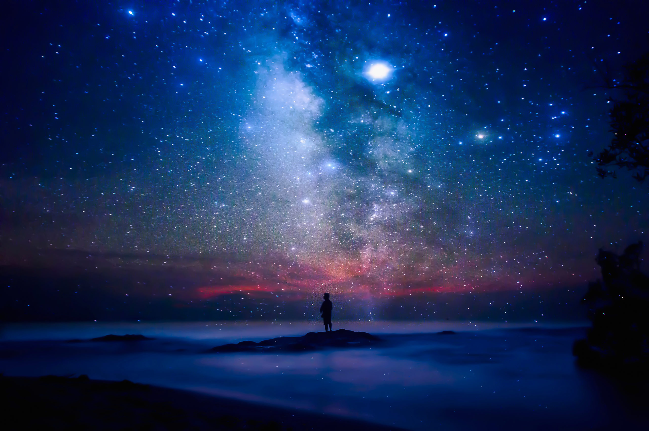 Starry night sky over sea and beach with man silhouette.