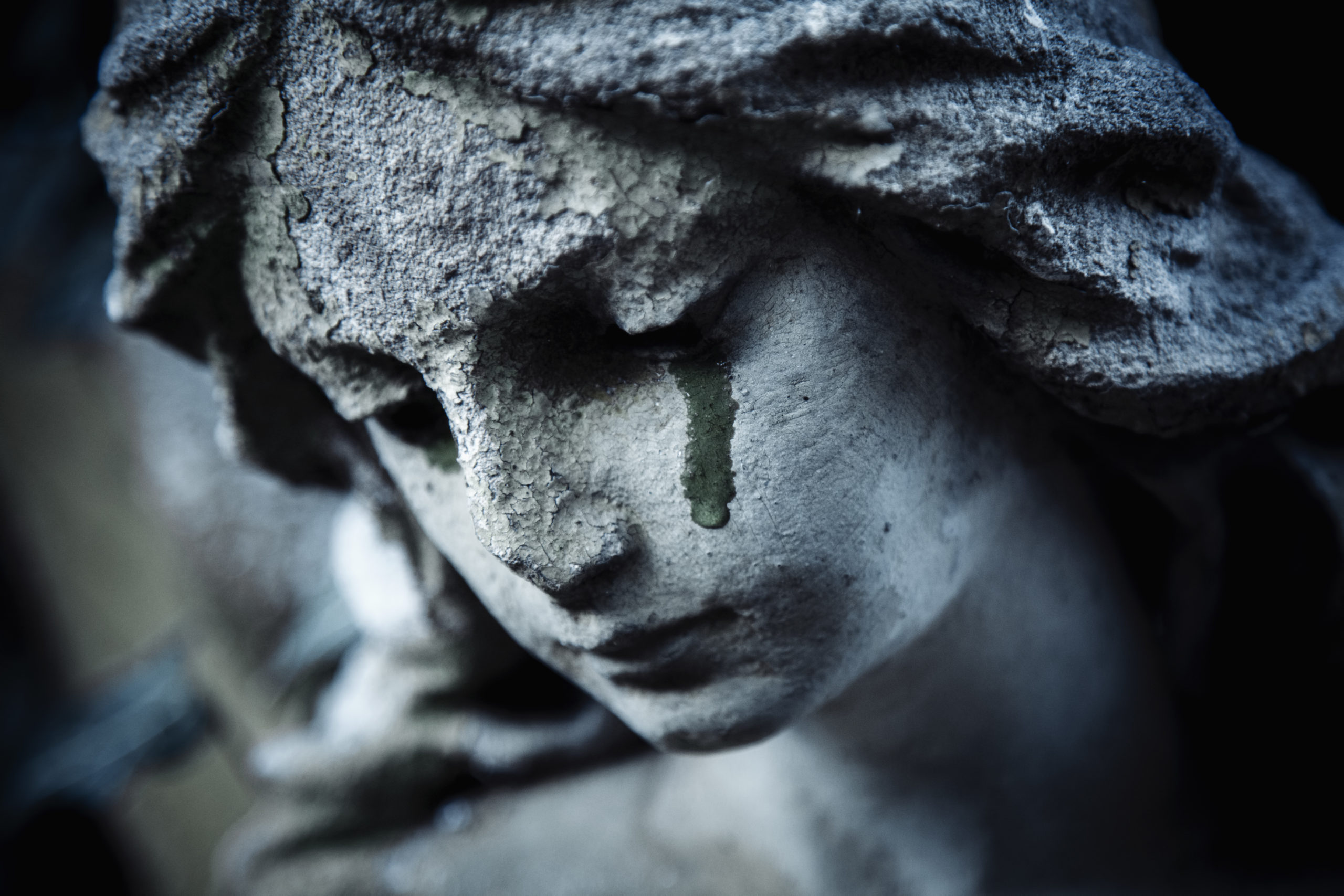 Ancient stone statue of crying sad angel with tears in face as symbol of death and end of human life.