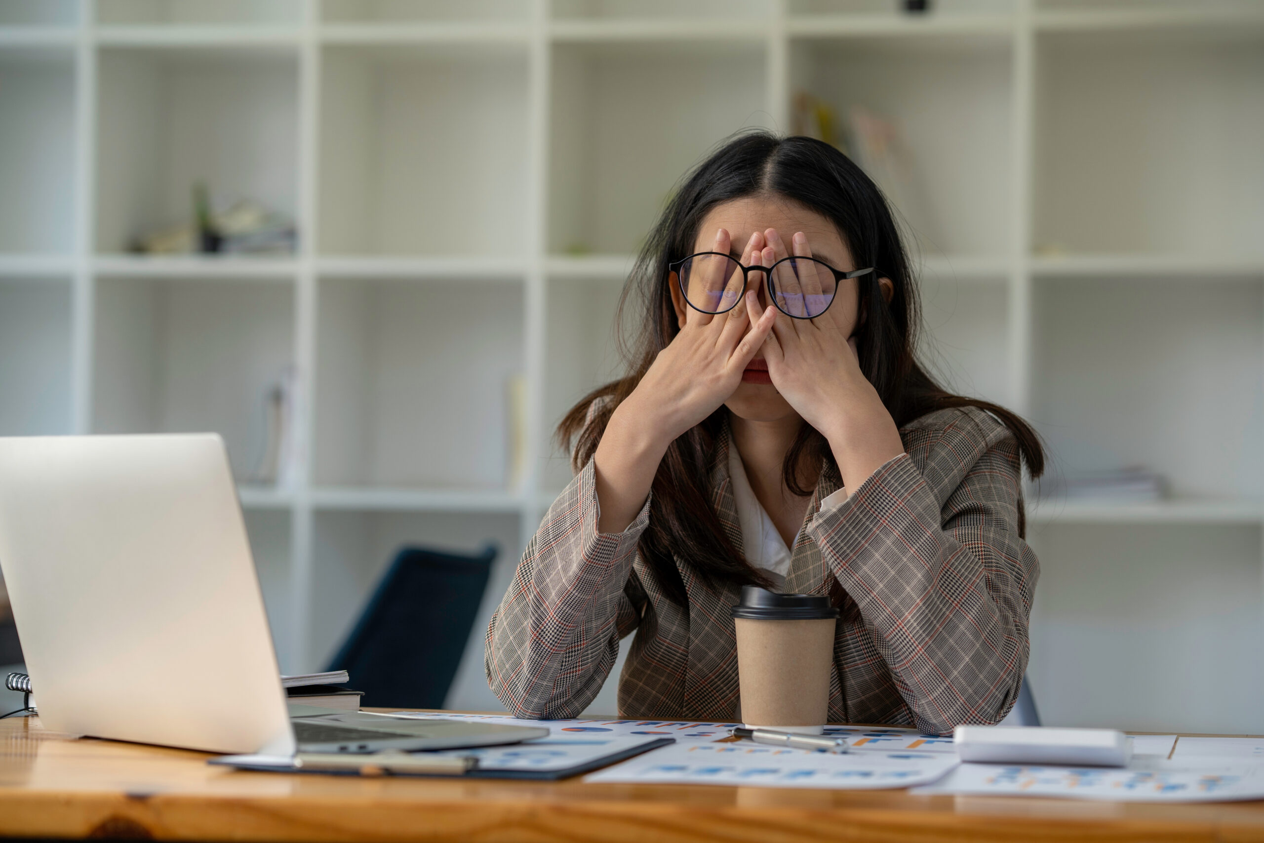 business woman sitting at a desk with hands to her face showing sadness or fatigue
