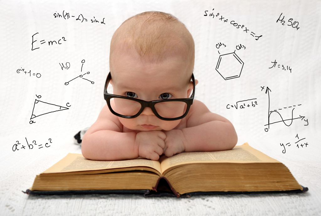 funny portrait of cute baby in glasses lieing on old book and thinking of all the knowledge in the world