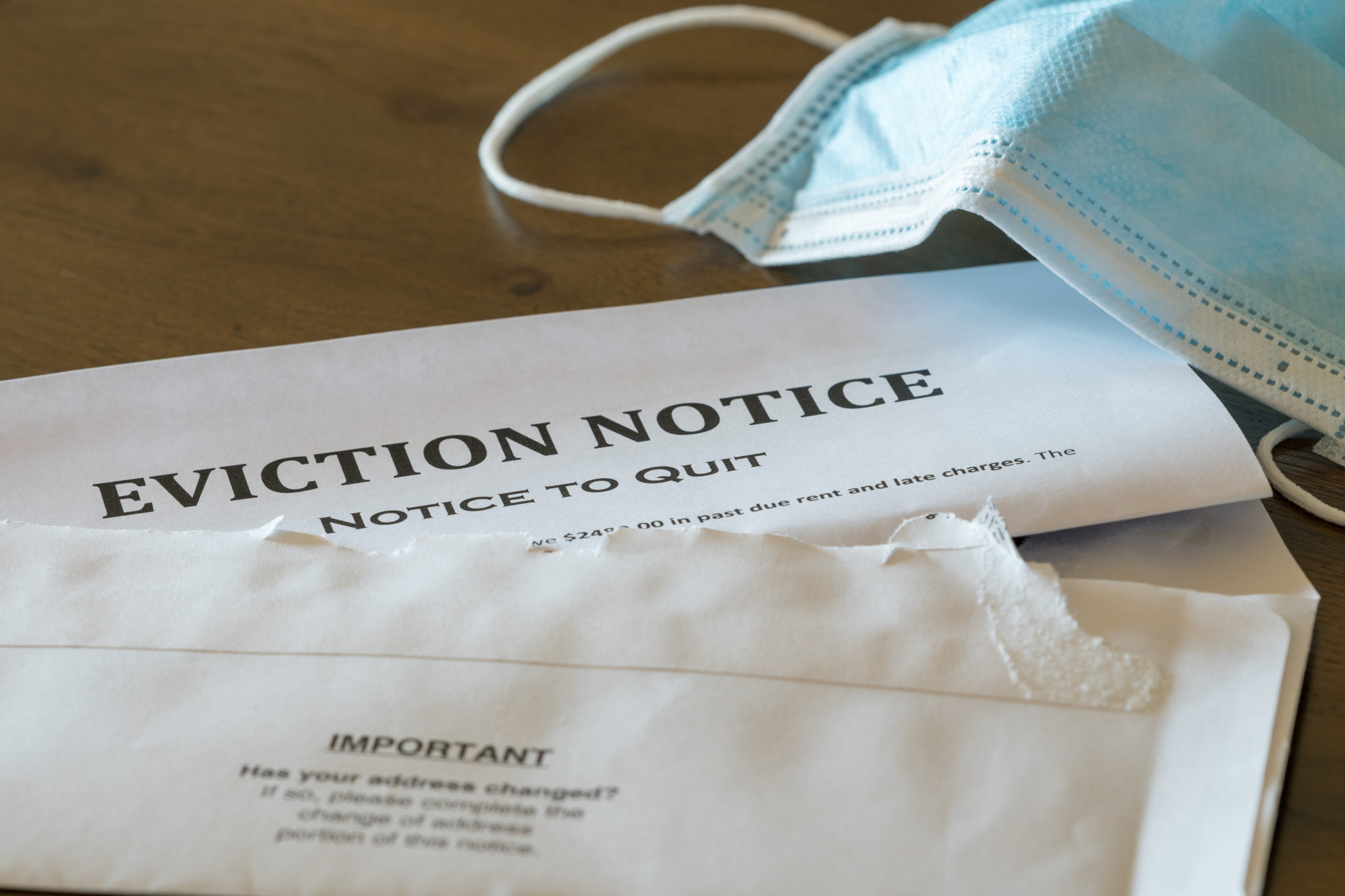 Defaulting renter with facemask receives letter giving notice of eviction from home on wooden table
