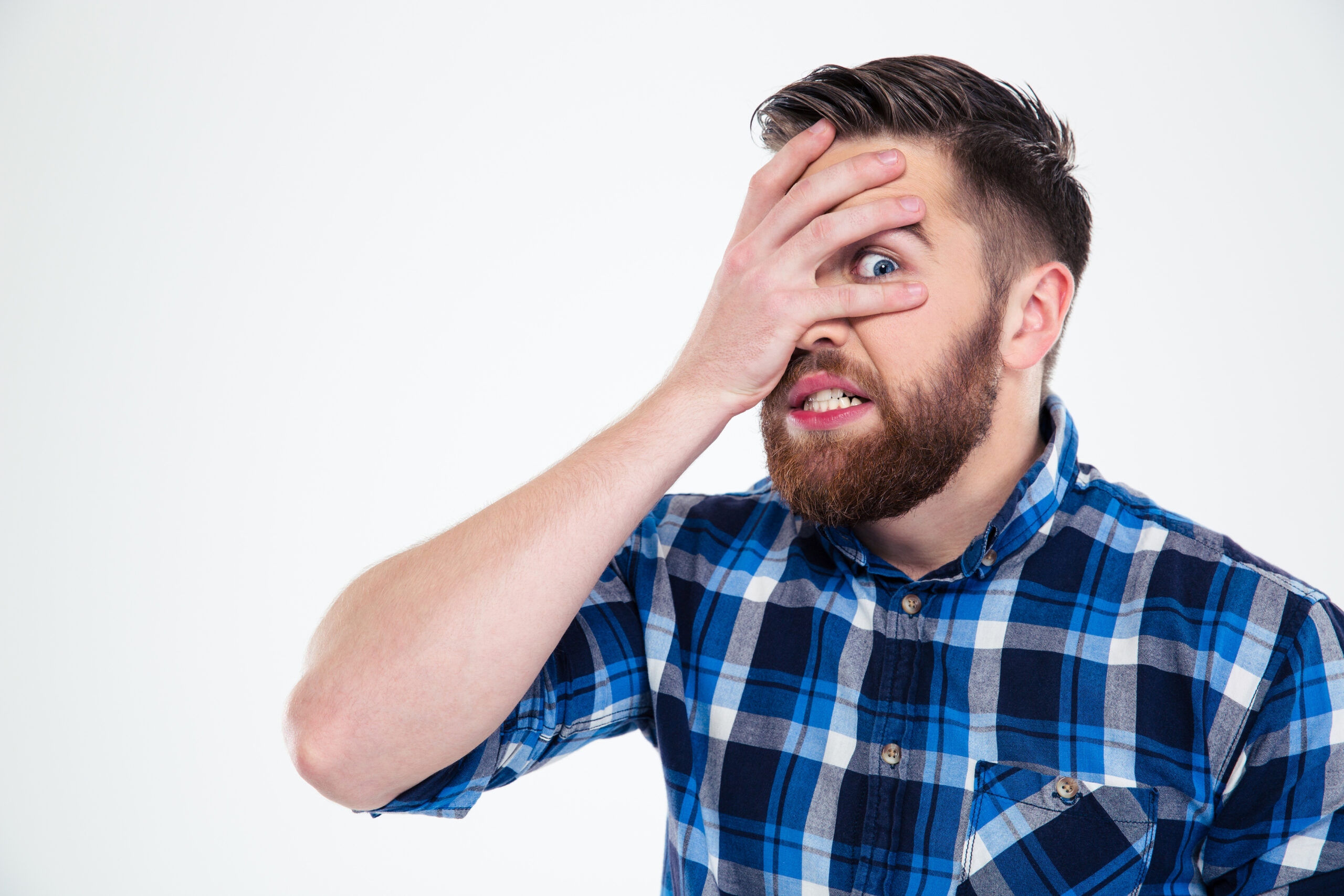 Portrait of a scared man covering his face with palm and looking at camera through fingers