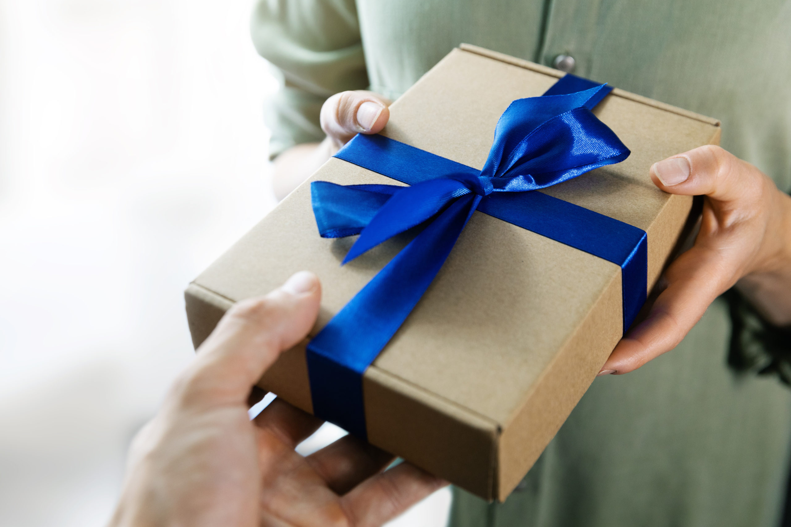 hand giving gift box with blue ribbon to a woman.
