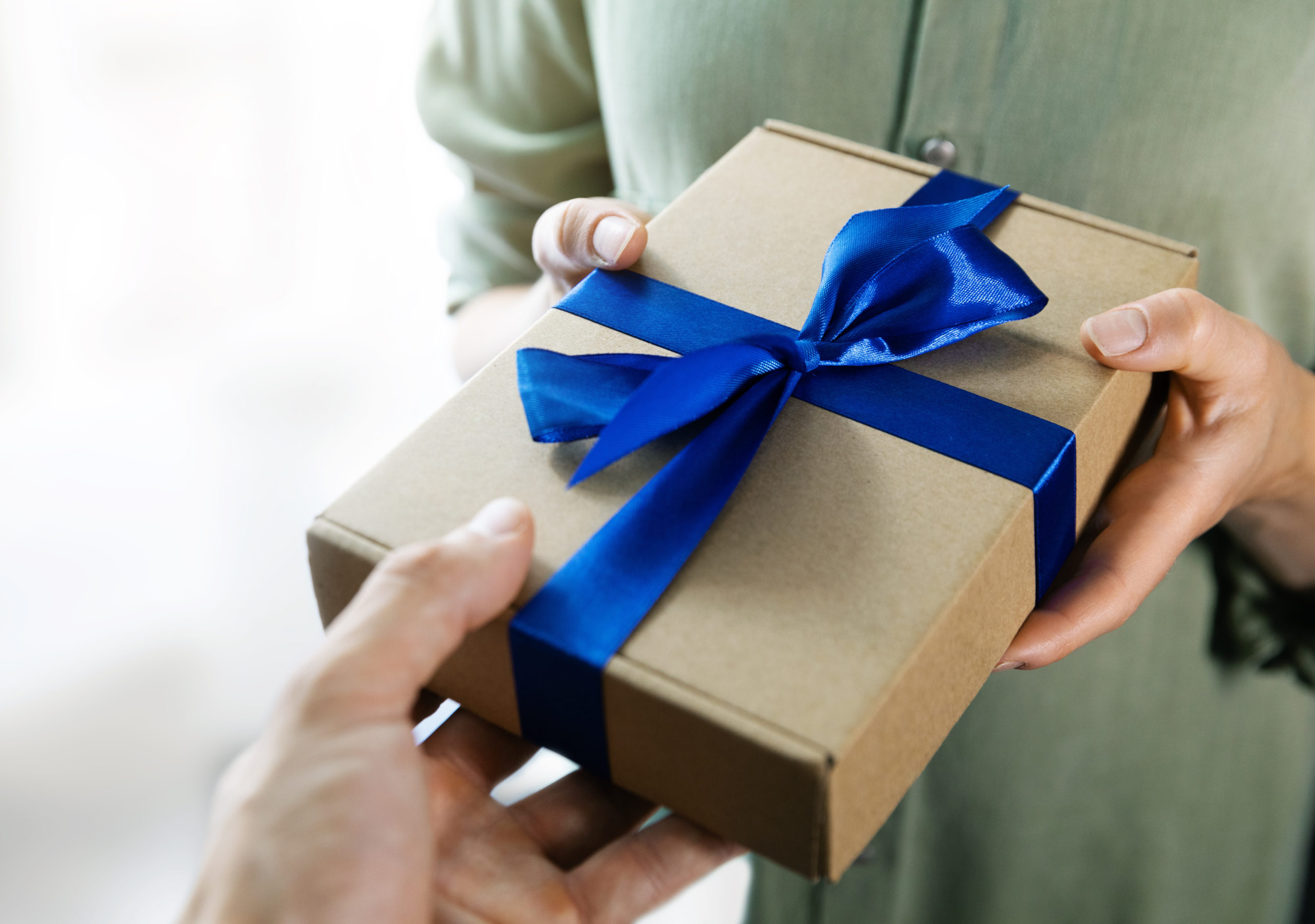 hand giving gift box with blue ribbon to a woman.