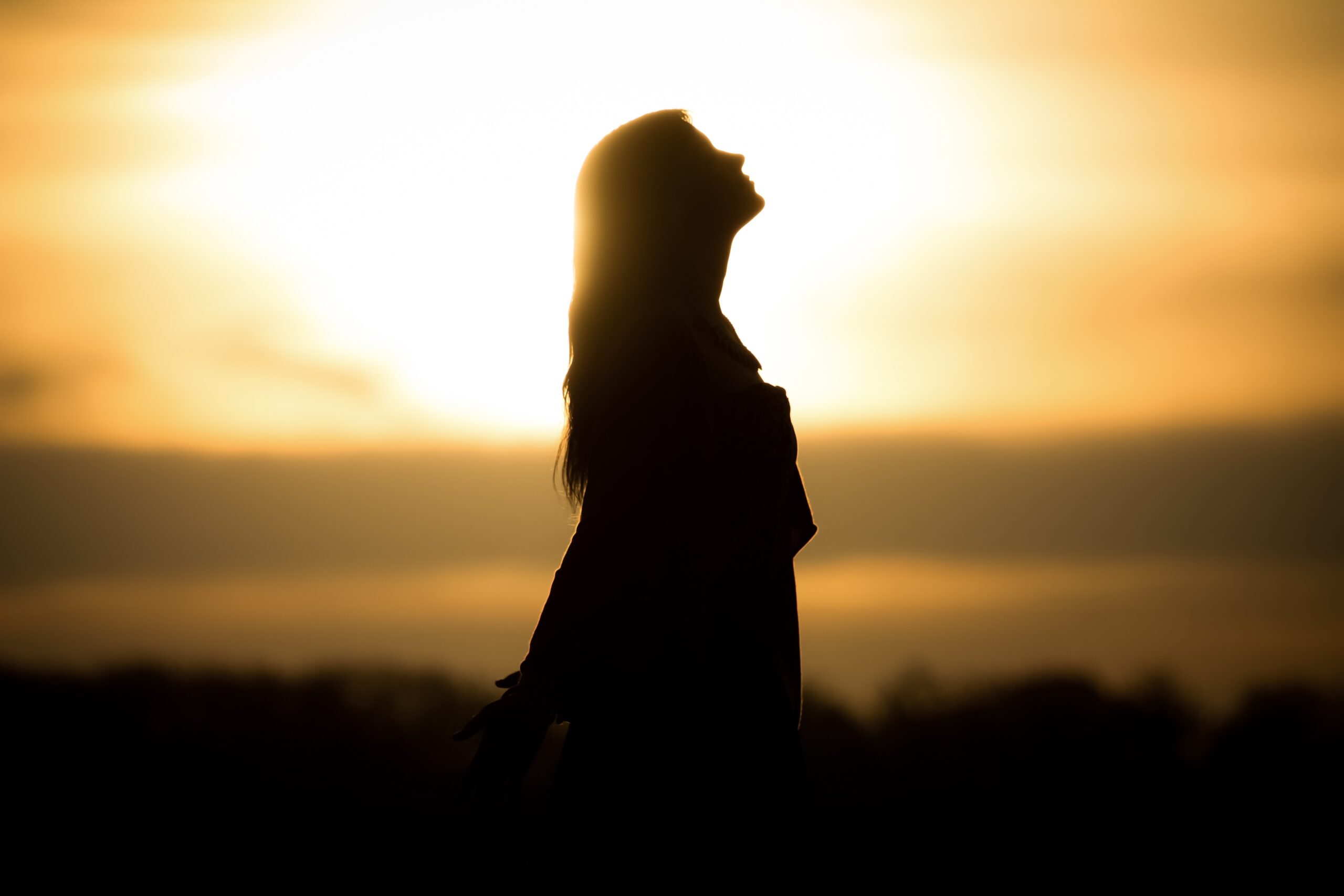 silhouette of woman meditating in foreground, sunrise or sunset in background