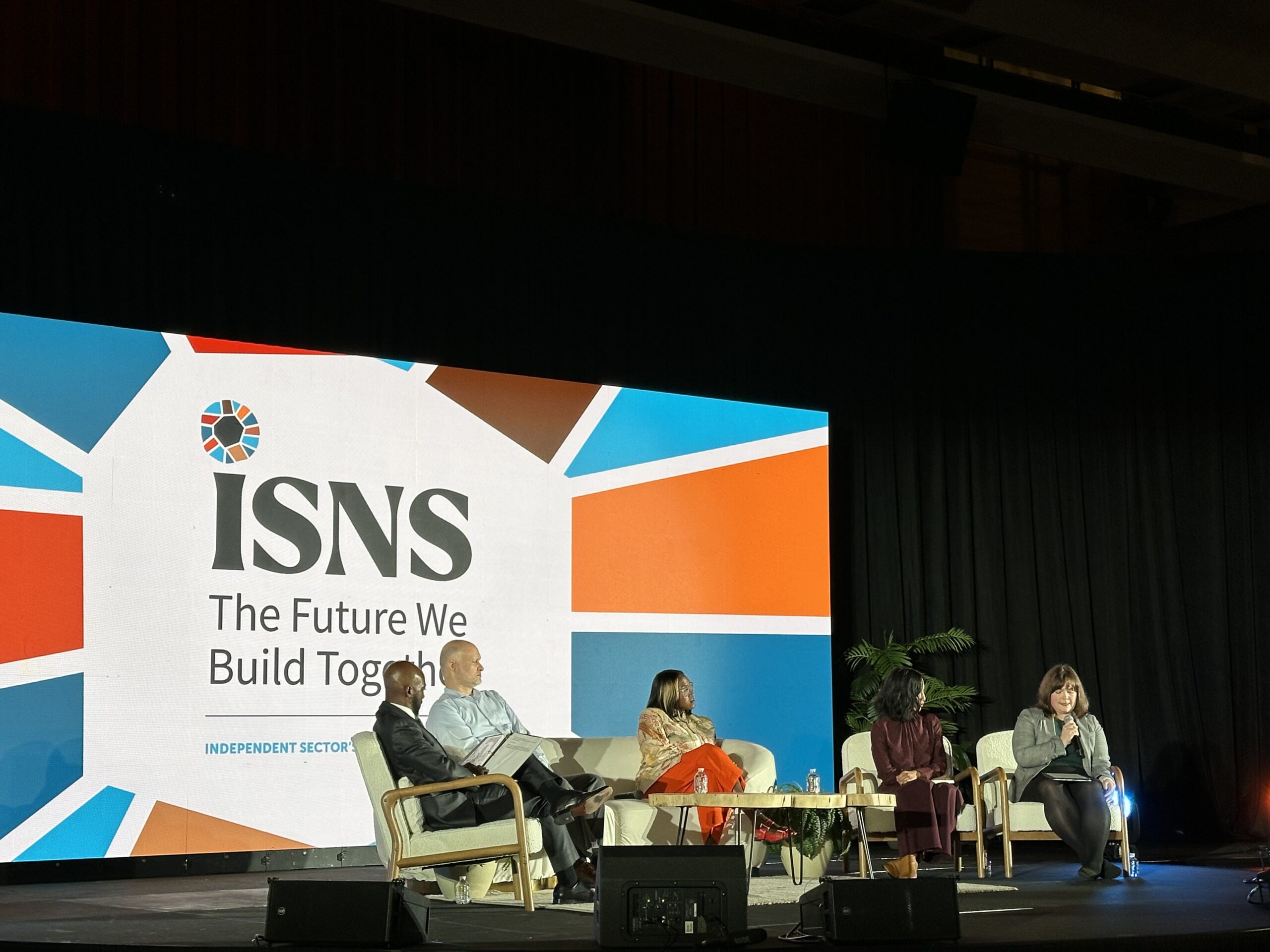 Photo from Independent Sector 2026 Summit featuring 5 persons sitting in a panel discussion in front of a videoscreen with the conference logo