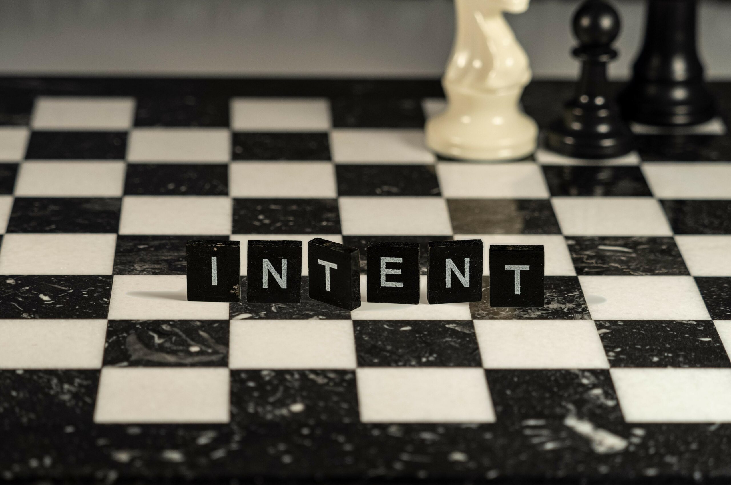 intent concept represented by black and white letter tiles on a marble chessboard with chess pieces