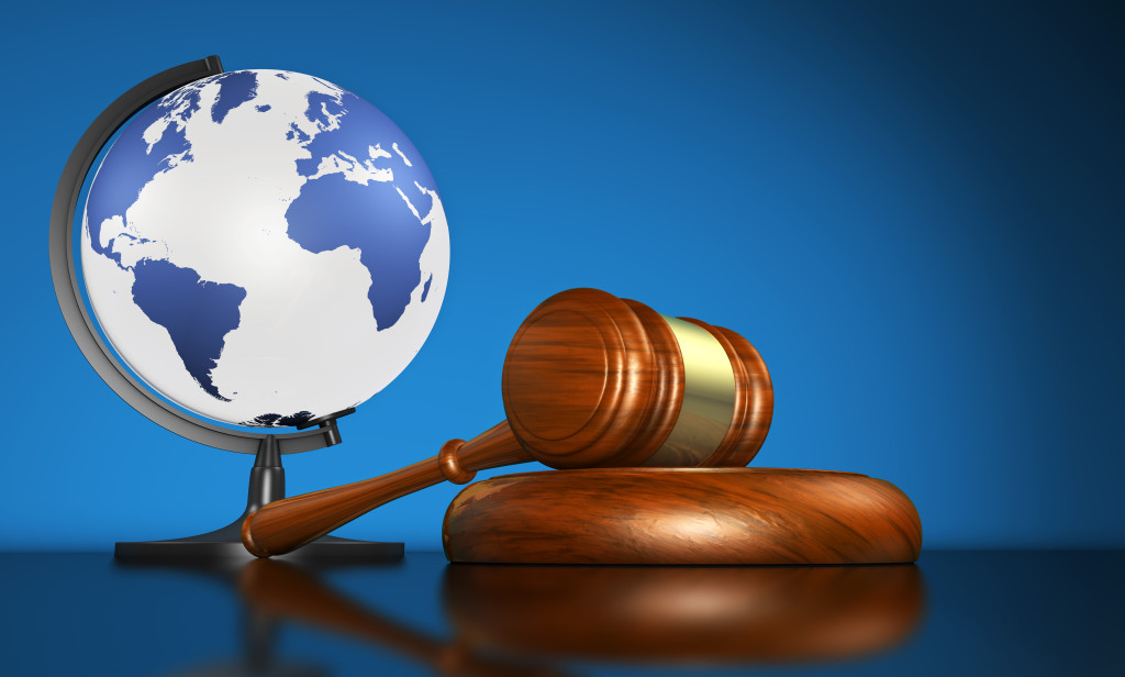 International law systems, justice, human rights and global business education concept with world map on a school globe and a gavel on a desk on blue background.
