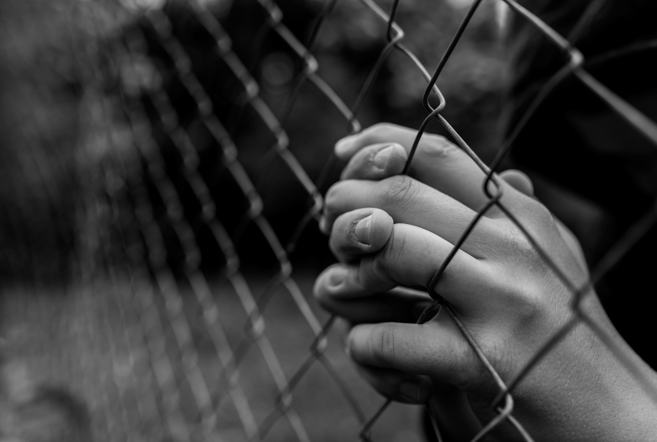 young looking hands praying behind a gate
