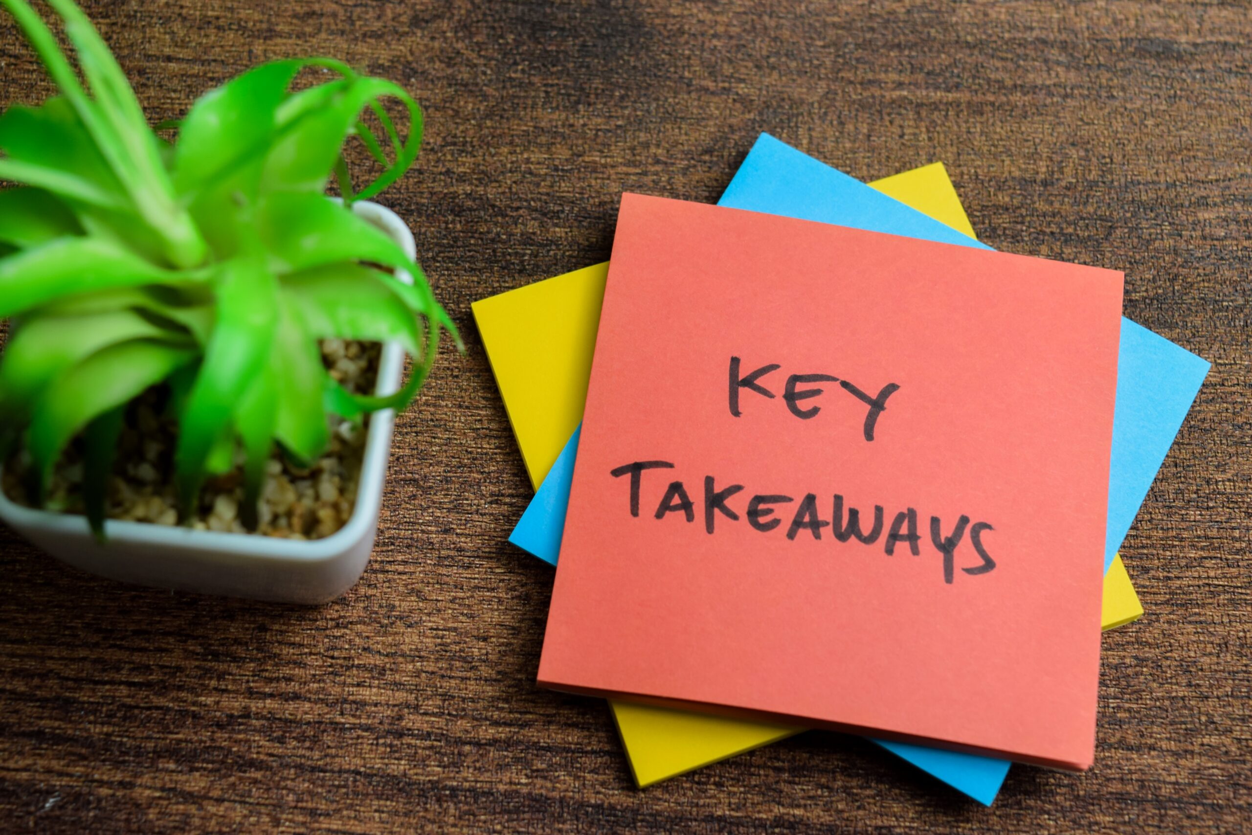 "Key Takeaways" written on post-it on wooden table with plant
