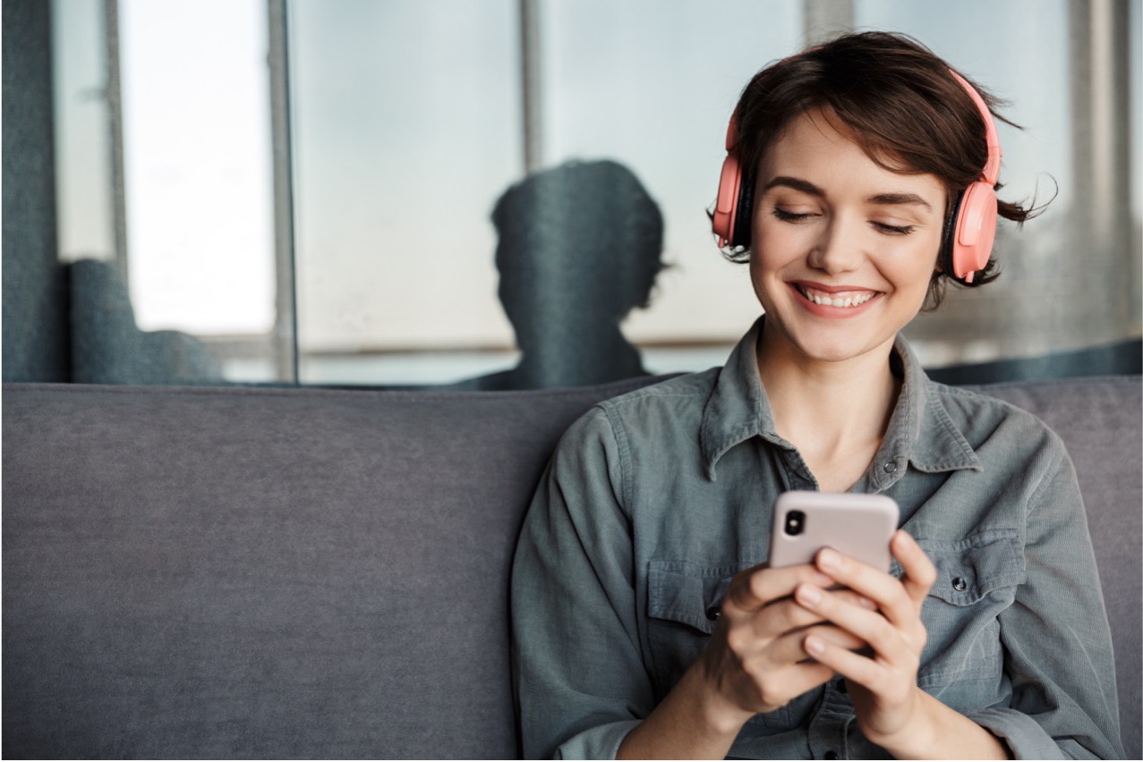 smiling woman listening on headphones connected to phone