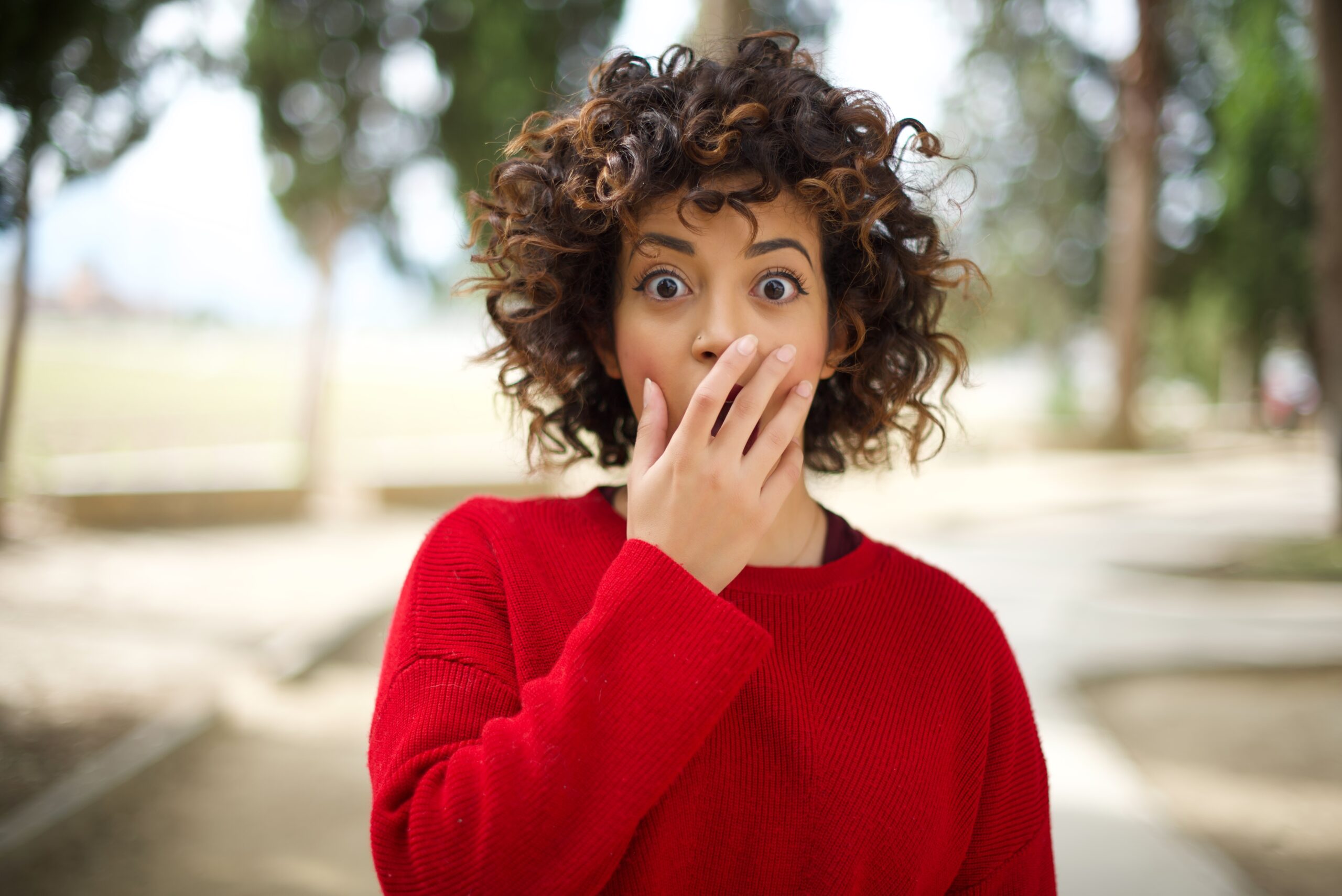 Woman wearing red sweater gasps with hand covering mouth