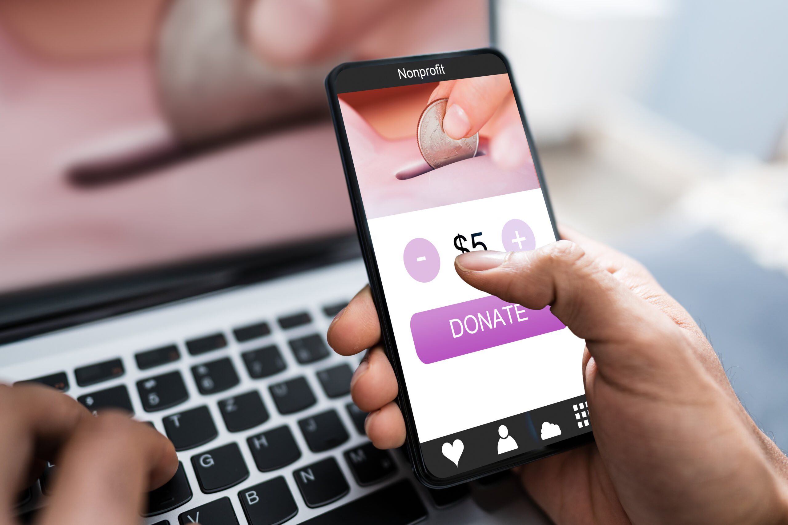 Hand Donating Money On Mobile Phone Over Laptop