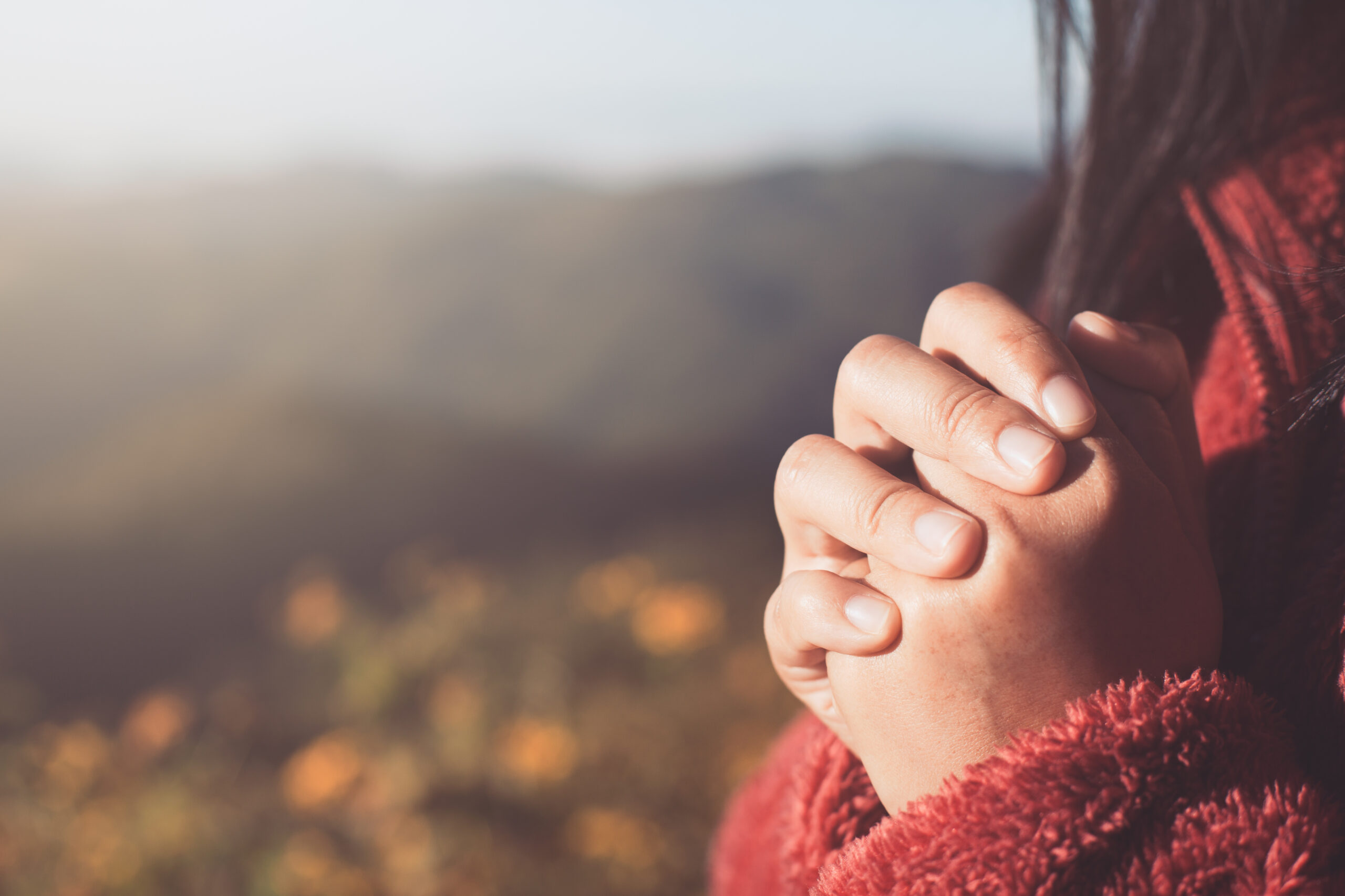 Woman or child's hands folded in prayer with a blurred nature background
