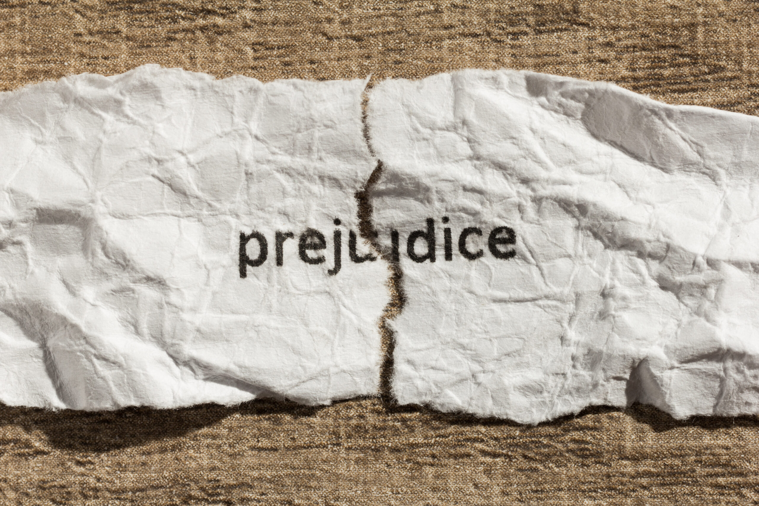 Torn paper with word "prejudice" written on it over wooden background