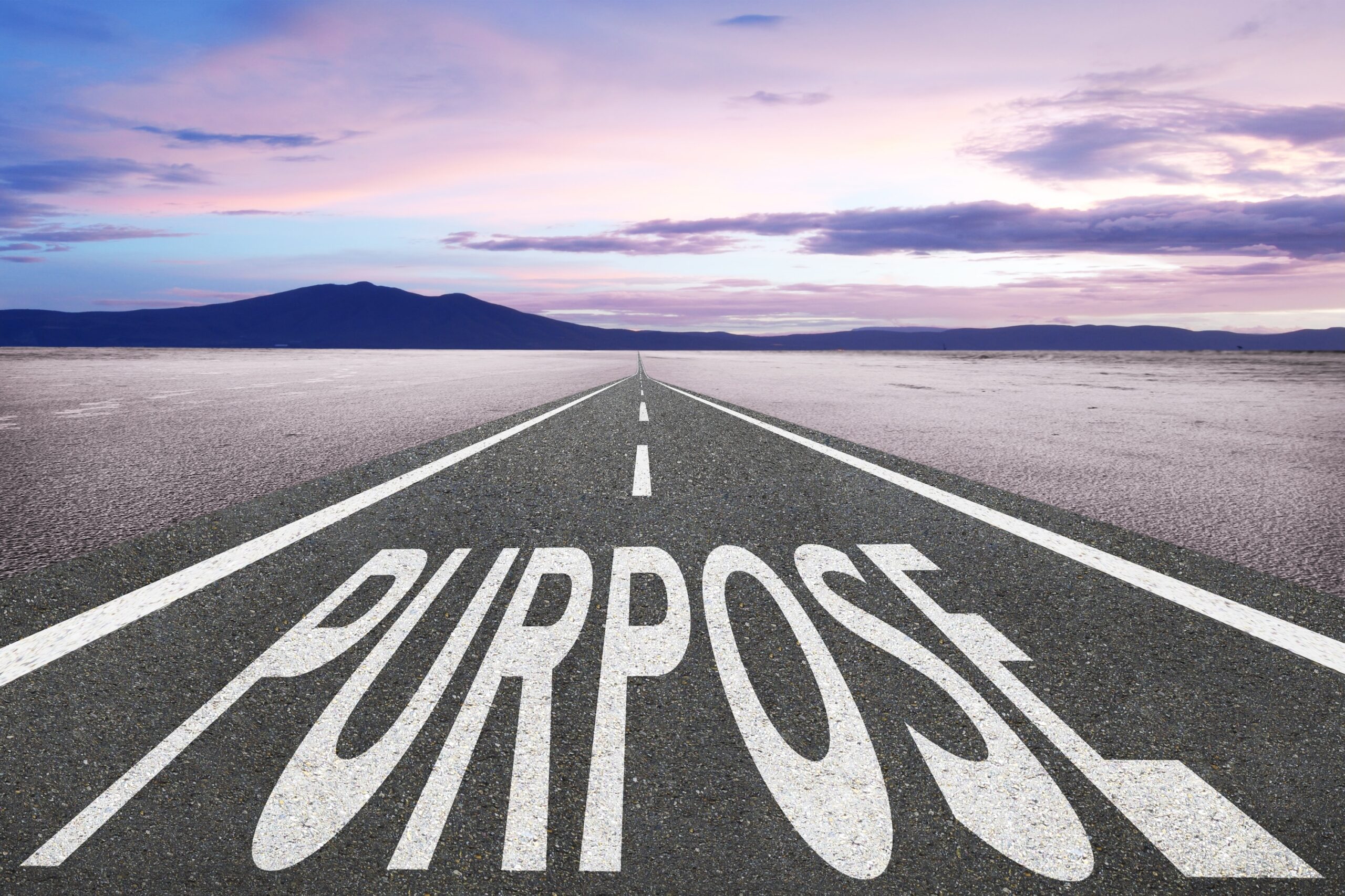 "PURPOSE" written on highway with sunset and mountains in far background