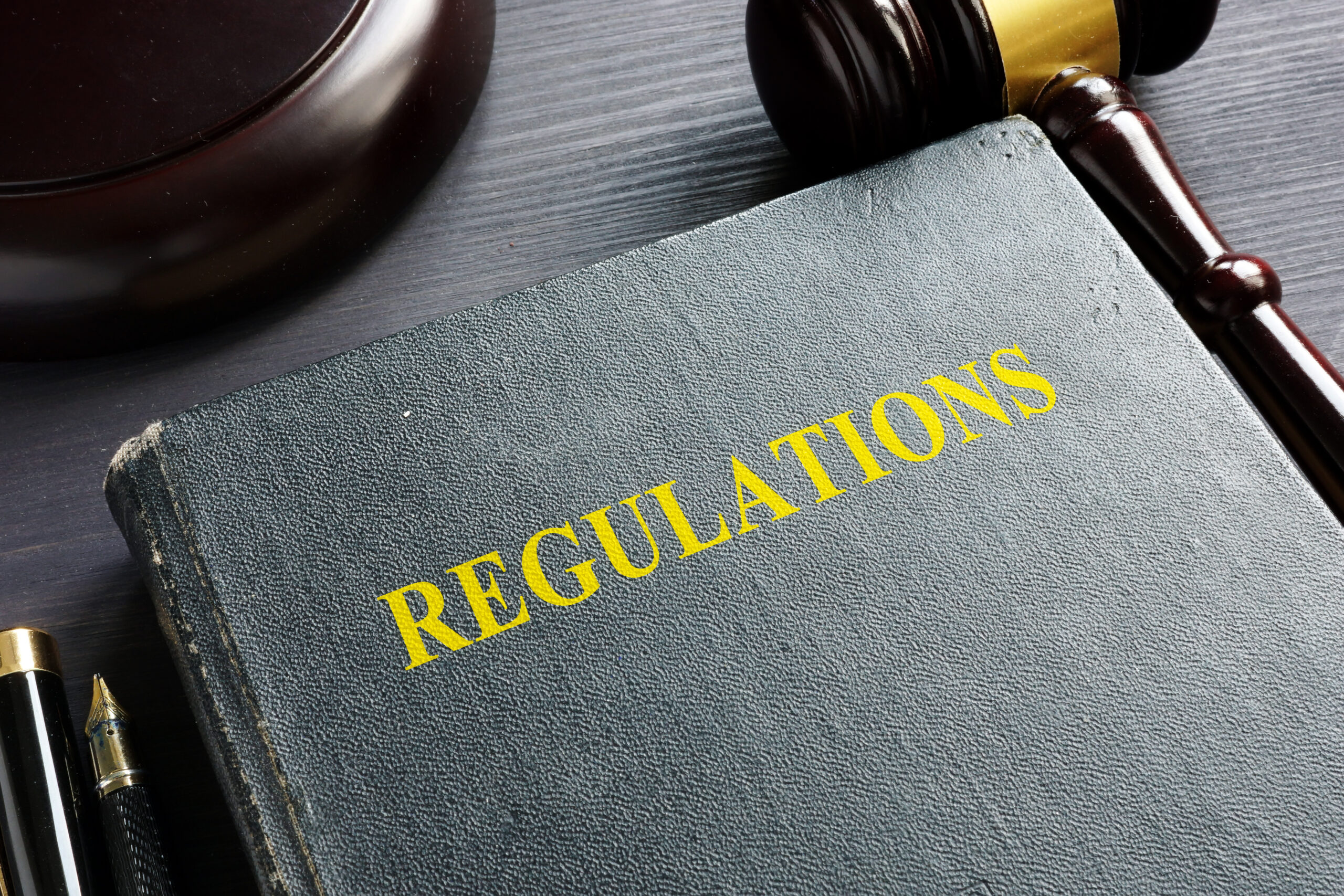 "Regulations" embossed on a book with gavel in background.