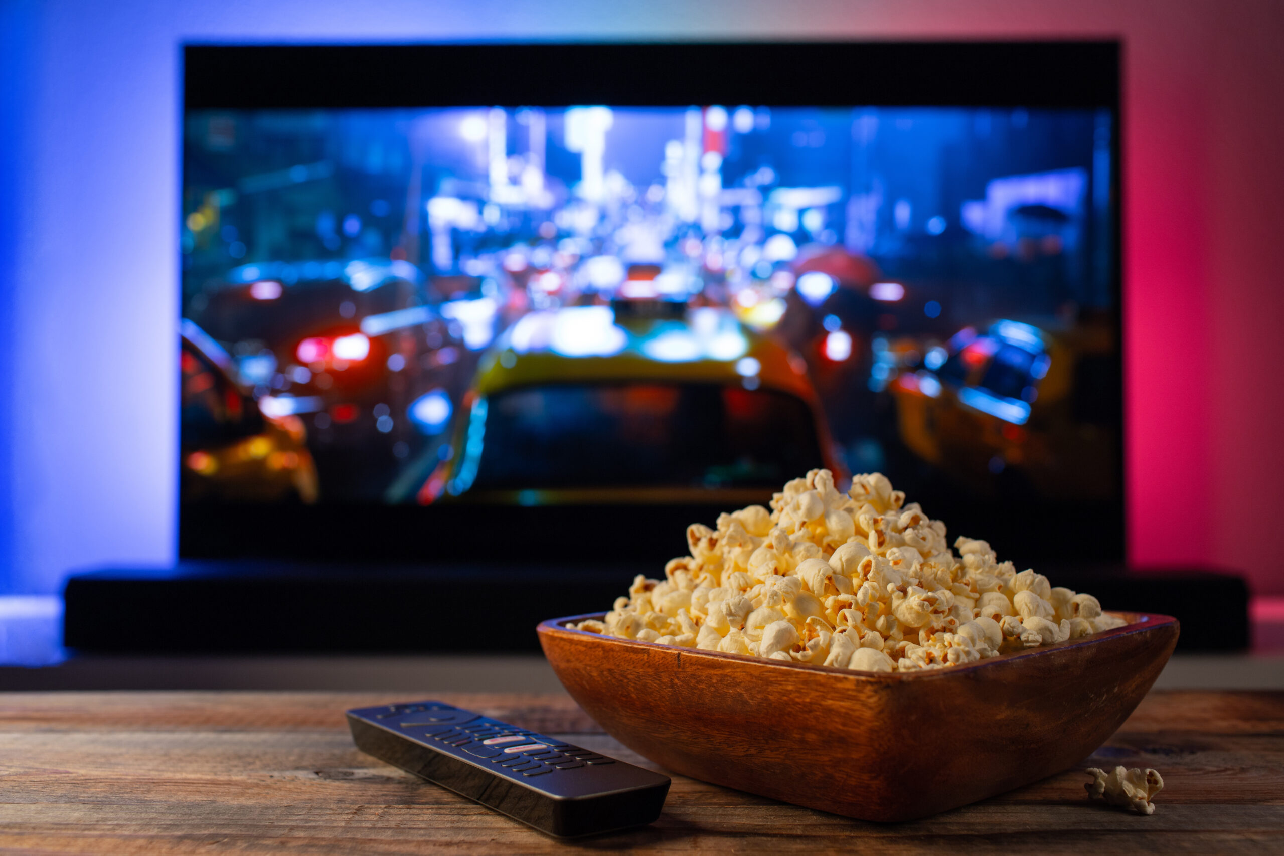 A wooden bowl of popcorn and remote control in the background - a big screen television.