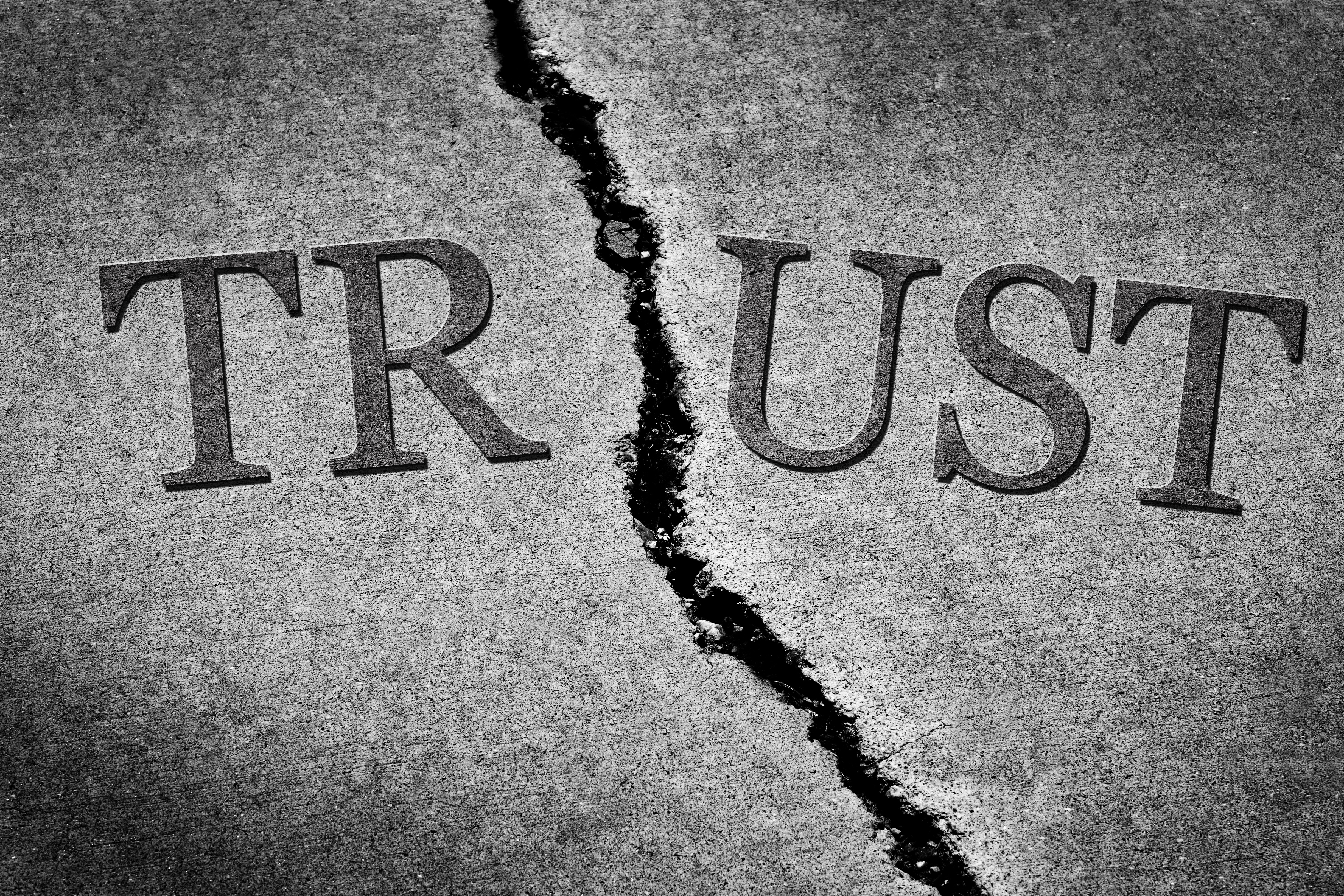 Old cracked sidewalk with the word "trust" cracked in half
