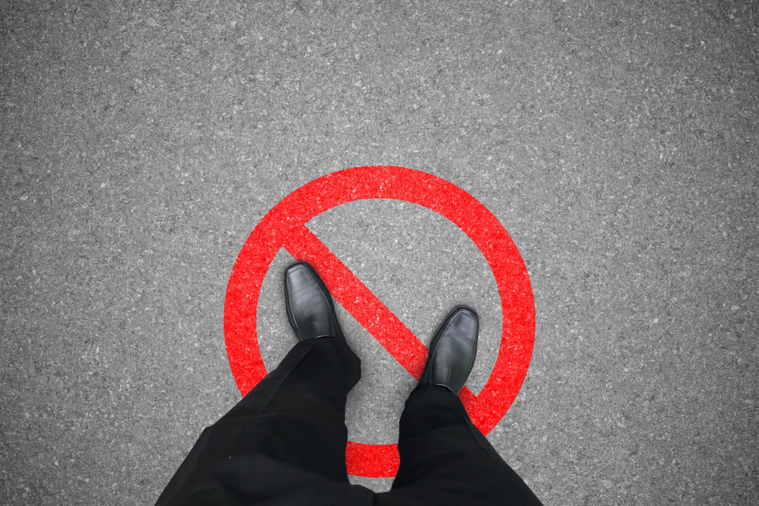 Businessperson in black shoes standing on red prohibited symbol.