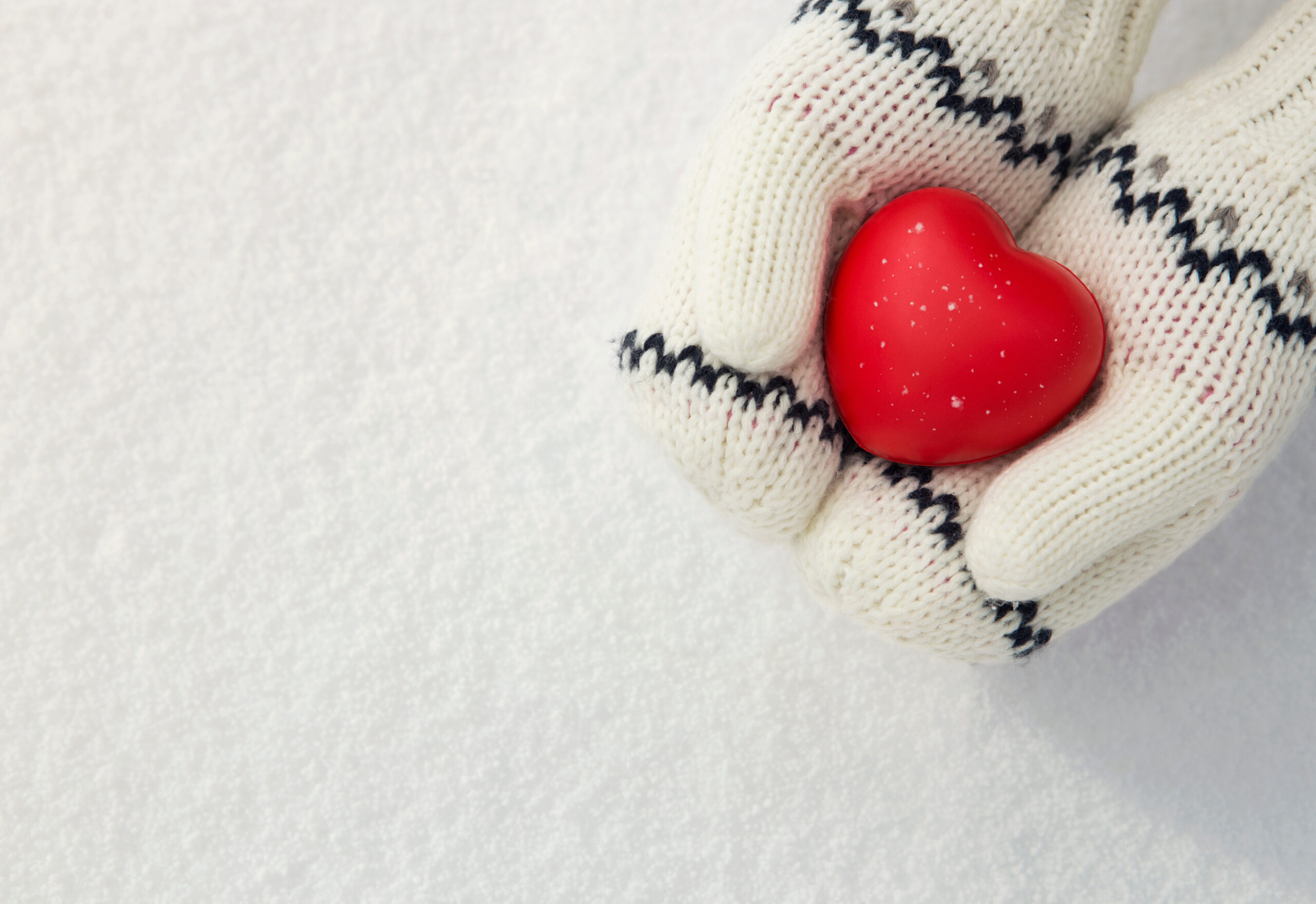 Close up of hands in white mittens holding red heart