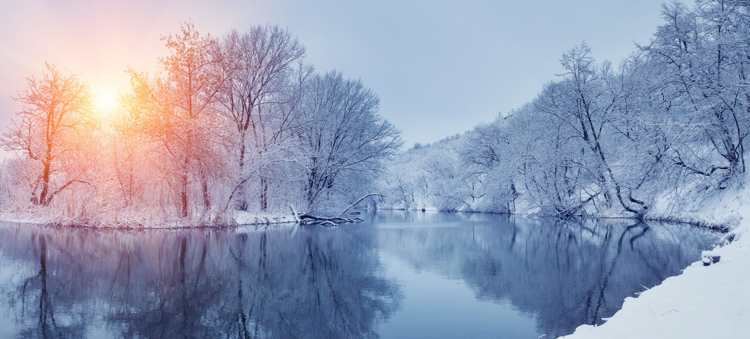Winter forest scene with lake in foreground and sunset in back