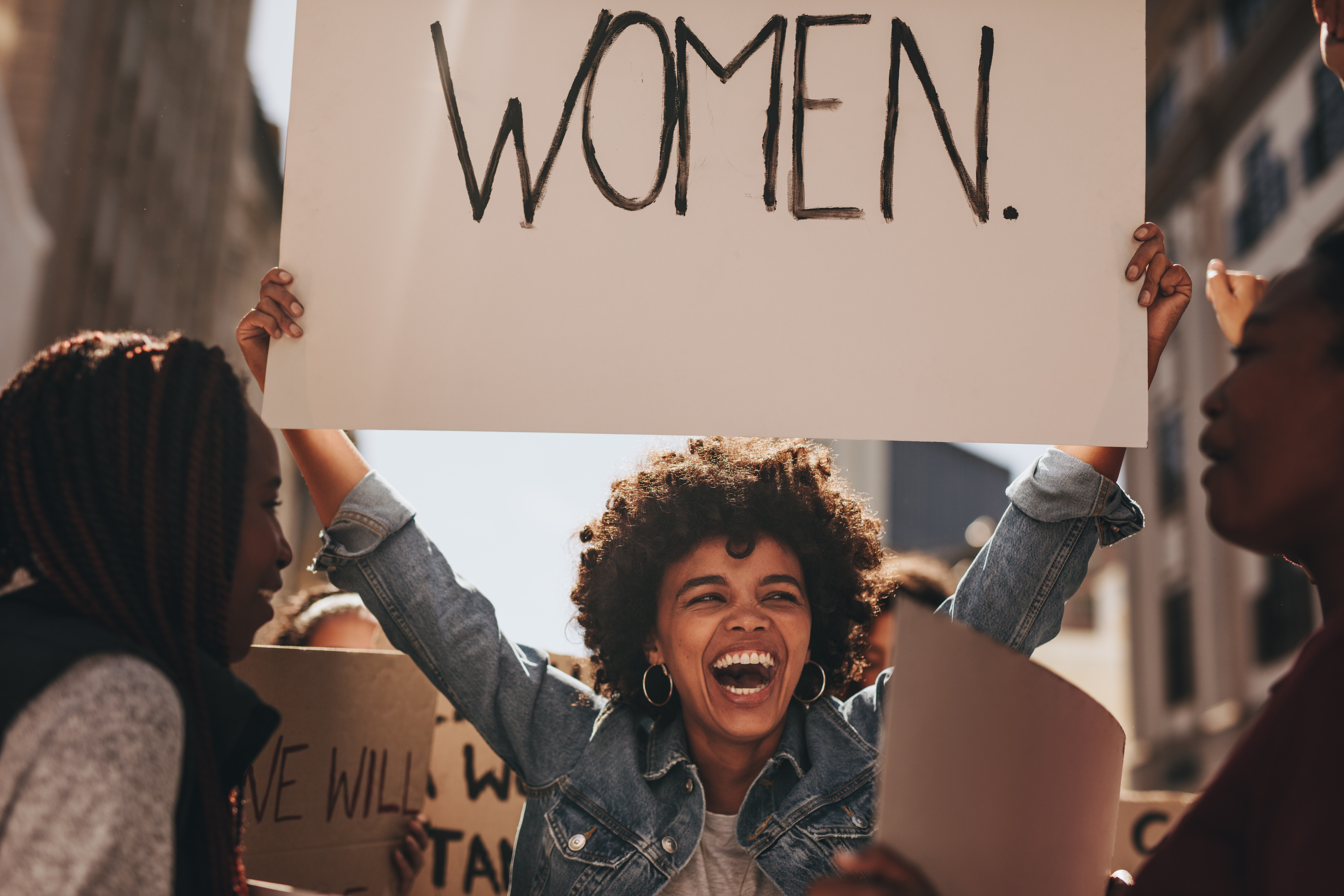 Laughing young woman holding a banner "WOMEN" during a protest.